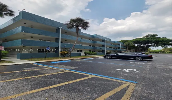 Three-story multi-unit structure featuring a textured blue facade, recessed balconies, and paved surface parking