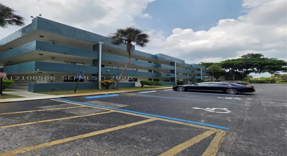 Three-story multi-unit structure featuring a textured blue facade, recessed balconies, and paved surface parking