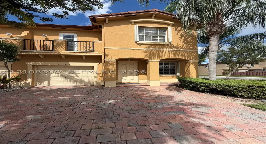 Stucco exterior featuring a paved driveway, covered entryway with arched columns, and a second-story balcony with metal railings