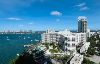 High-rise residential exterior with waterfront orientation, featuring an outdoor swimming pool, paved pedestrian pathways, lush landscaping, and integrated parking facilities