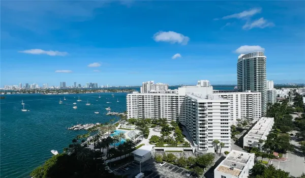 High-rise residential exterior with waterfront orientation, featuring an outdoor swimming pool, paved pedestrian pathways, lush landscaping, and integrated parking facilities