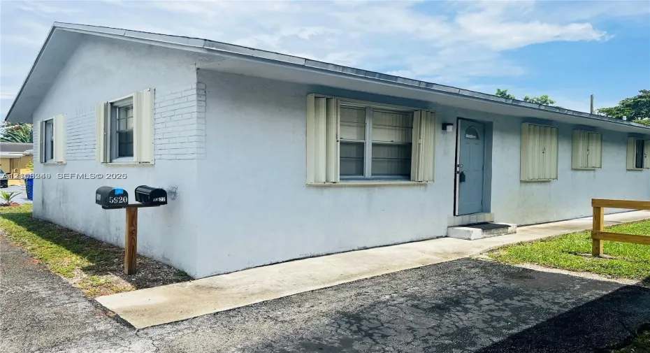 Stucco exterior featuring accordion hurricane shutters, a concrete walkway, and paved surface area