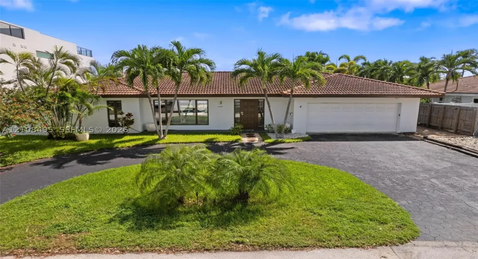 Single-story exterior featuring white stucco siding, a tiled roof, a multi-car garage, and a paved circular driveway
