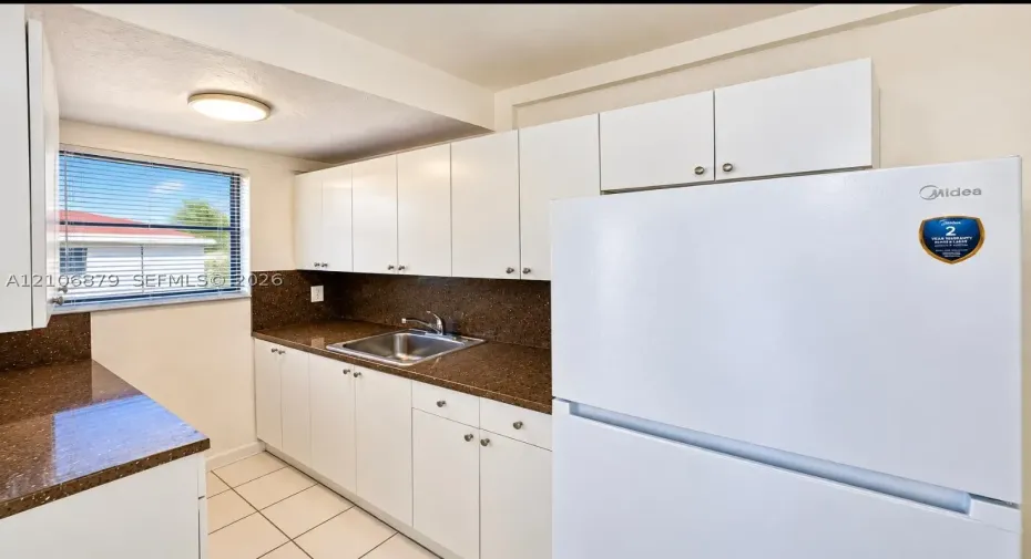 Kitchen featuring white cabinetry, dark stone-finish countertops, stainless steel sink with metal faucet, and tile flooring