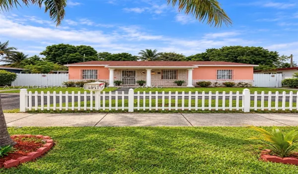 Single-story residence featuring a covered front porch with classic columns, white picket fencing, decorative stone masonry exterior, and side yard enclosures
