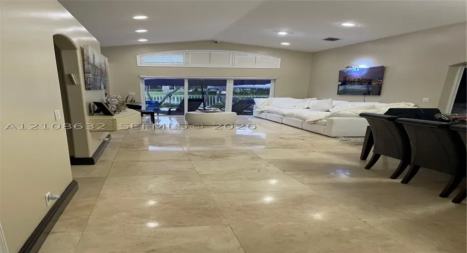 Spacious interior featuring large-format stone-style tile flooring, vaulted ceilings, recessed lighting, and an arched transom window above glass sliding doors