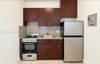 Kitchenette featuring deep-toned cabinetry, speckled stone-finish countertops, a stainless steel electric range, a stainless steel refrigerator, and a stainless steel sink with a mounted faucet