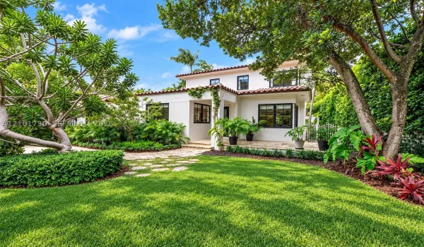 Two-story exterior featuring white stucco walls, dark-framed windows, and a terracotta tile roof, complemented by a stone paver patio and mature landscape