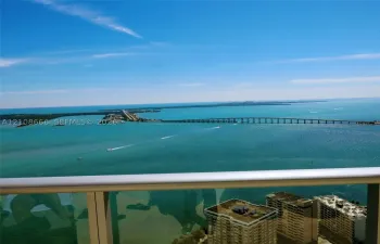 High-rise balcony featuring a metal railing with glass panels, showcasing panoramic coastal scenery, open water, and a bridge