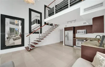 Double-height living area featuring an open staircase with wood treads and horizontal metal railings, tile flooring, built-in cabinetry, and integrated stainless steel appliances