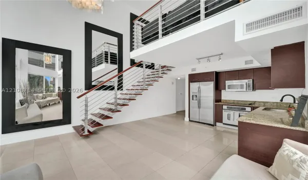Double-height living area featuring an open staircase with wood treads and horizontal metal railings, tile flooring, built-in cabinetry, and integrated stainless steel appliances