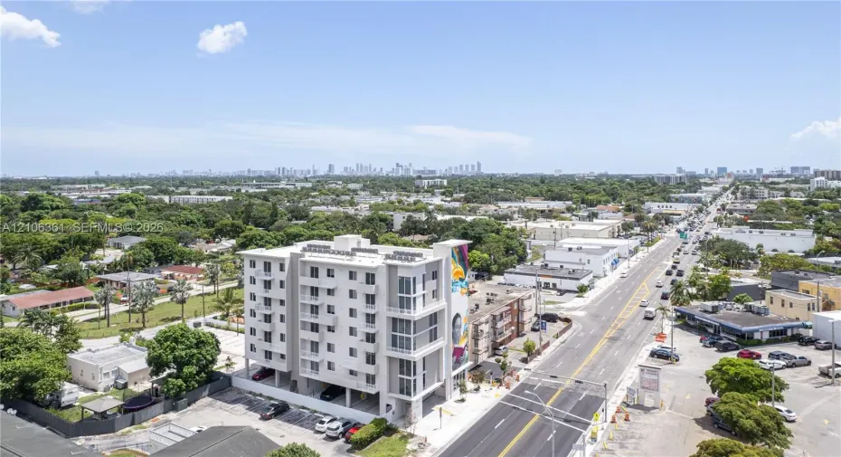 Mid-rise residential building featuring multi-level balconies, ground-level parking, and a prominent exterior mural