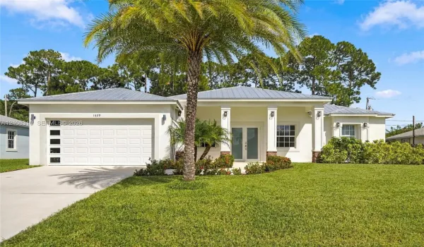 Stucco exterior residence featuring a metal roof, double-entry front doors with glass inserts, a two-car garage with horizontal window panels, and decorative stone-base columns