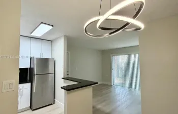 Contemporary kitchen featuring white cabinetry, a stainless steel refrigerator, dark stone-finish countertops, and a modern circular LED pendant light fixture