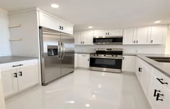 Kitchen featuring white shaker-style cabinetry, quartz countertops, stainless steel appliances, vertical tile backsplash, and polished tile flooring