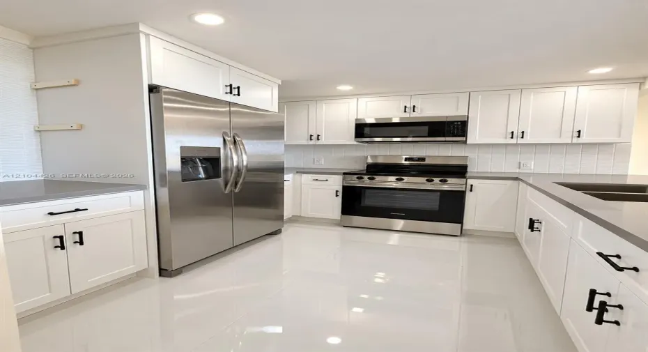 Kitchen featuring white shaker-style cabinetry, quartz countertops, stainless steel appliances, vertical tile backsplash, and polished tile flooring