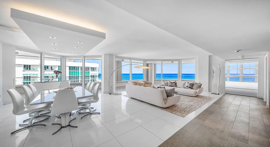 Open-concept interior featuring floor-to-ceiling glass windows, ocean scenery, white tile flooring, and a recessed ceiling architectural detail with integrated lighting