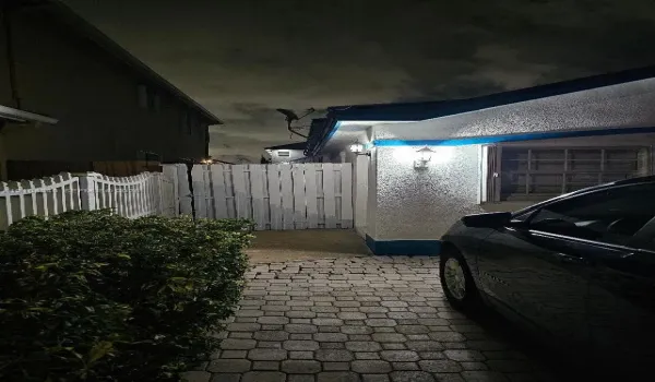 Textured stucco exterior featuring stone paver driveway, white privacy fencing, and exterior wall-mounted light fixtures