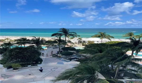 Oceanfront balcony perspective featuring tropical landscaping, expansive resort-style pools, stone-paved walkways, and immediate access to the coastline