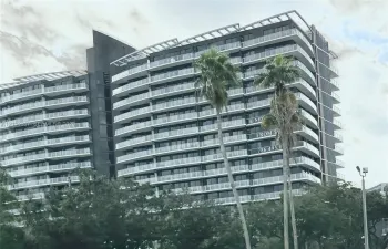 Modern high-rise exterior featuring a dark metallic facade, rhythmic rows of glass-railed balconies, and a stepped roofline