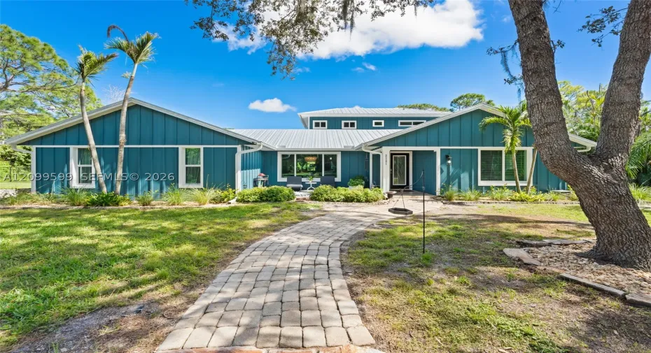 Single-story residence featuring vertical board siding, a metal roof, a stone paver walkway, and mature landscaping