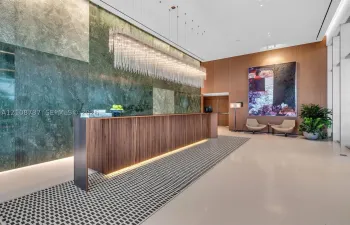 Grand lobby featuring a floor-to-ceiling polished stone accent wall, custom wood-finish reception desk with integrated lighting, elongated linear crystal chandelier, and large-format tile flooring