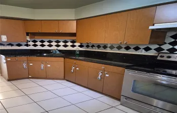 Kitchen featuring wooden cabinetry, dark stone-finish countertops, stainless steel range, and a black and white diamond-pattern tile backsplash
