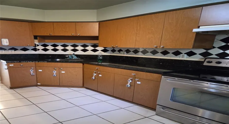 Kitchen featuring wooden cabinetry, dark stone-finish countertops, stainless steel range, and a black and white diamond-pattern tile backsplash