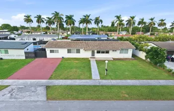 Single-story exterior featuring a light-colored stucco finish, tiled roof, paved driveway, and a concrete walkway leading to the entrance