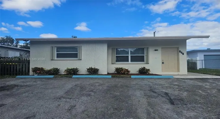 Single-story exterior featuring a light-toned masonry facade, overhanging roofline, horizontal sliding windows with trim, and concrete parking area