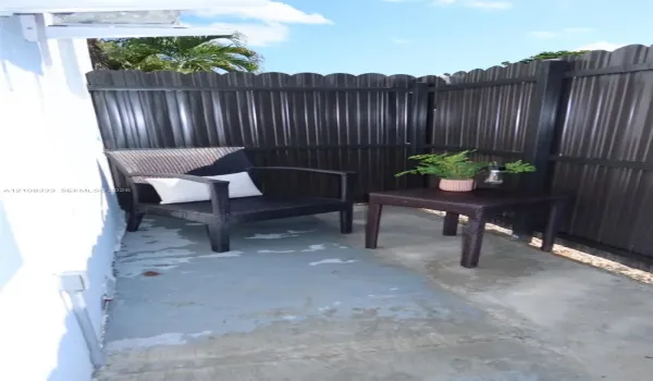 Enclosed patio featuring a concrete floor and a full-height corrugated metal privacy fence