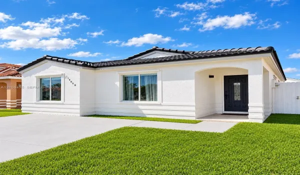 Stucco exterior featuring horizontal banding, a dark-toned tile roof, dual-pane windows, a recessed entry with a paneled front door, and a concrete driveway