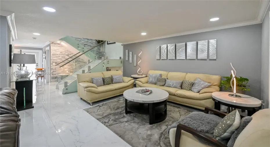 Polished porcelain tile flooring, recessed ceiling lighting, and a staircase featuring glass panels with metal railings and a textured stone accent wall