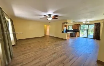 Open-concept interior featuring wood-finish tile flooring, a palm-leaf style ceiling fan, dark cabinetry, and sliding glass doors
