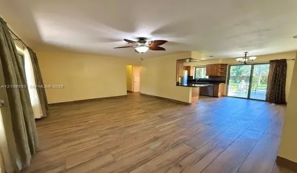 Open-concept interior featuring wood-finish tile flooring, a palm-leaf style ceiling fan, dark cabinetry, and sliding glass doors