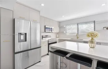 Kitchen featuring flat-panel cabinetry with gold-tone hardware, a central island with a solid-surface countertop, stainless steel appliances, and recessed lighting