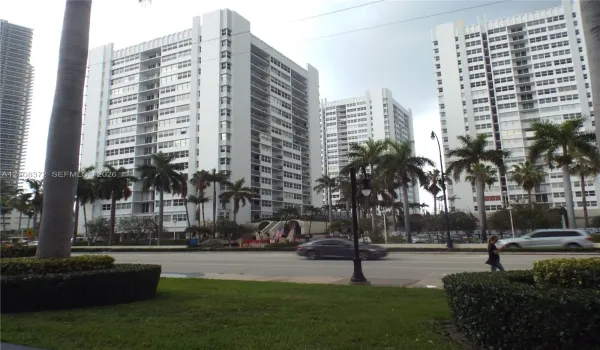 Multi-story high-rise architecture featuring white concrete facade, grid-patterned balconies, floor-to-ceiling windows, and surrounding palm tree landscaping