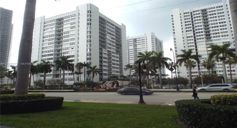 Multi-story high-rise architecture featuring white concrete facade, grid-patterned balconies, floor-to-ceiling windows, and surrounding palm tree landscaping