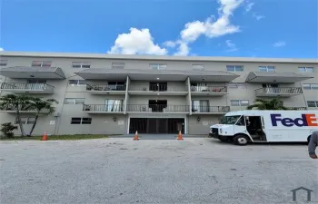Multi-story residential building exterior featuring concrete facade, private metal-railed balconies, and a secured gated entryway