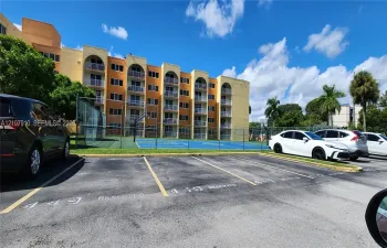 Multi-story exterior featuring arched balconies, an asphalt parking lot, and a fenced basketball court