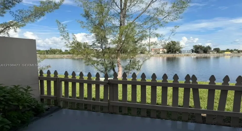 Concrete patio featuring a picket fence, manicured lawn, and water frontage
