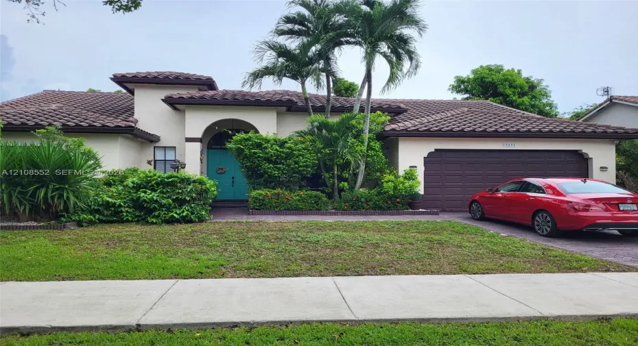 Stucco exterior featuring a multi-gabled clay tile roof, arched entryway, and attached multi-car garage
