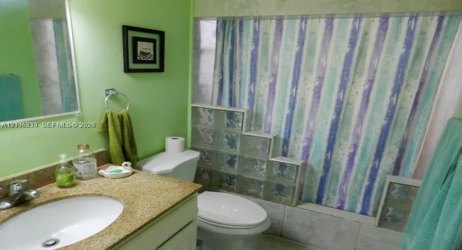 Bathroom featuring a vanity with an integrated basin, stone-composite countertop, wall-mounted mirror, and decorative glass block partition surrounding the shower area