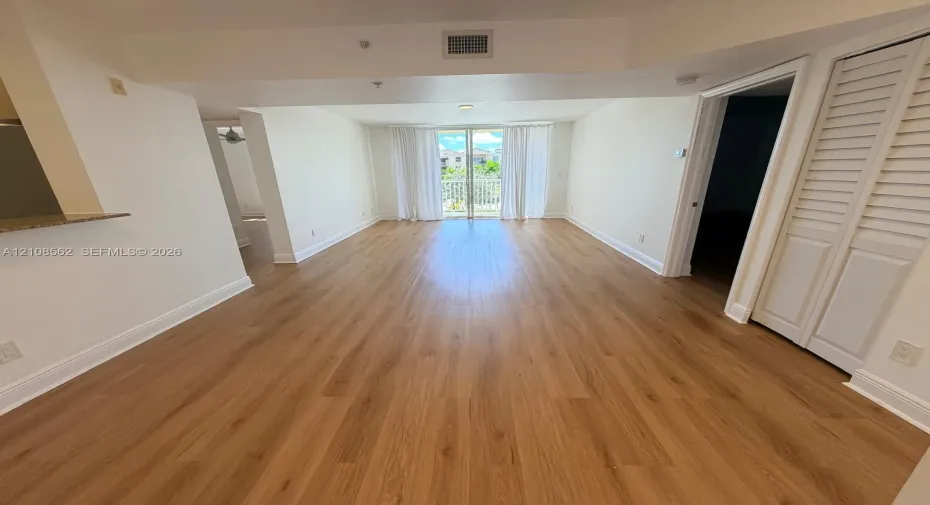 Open-concept interior featuring wood-finish flooring, louvered closet doors, and a glass-paneled sliding door opening to a balcony