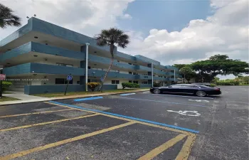 Three-story multi-unit structure featuring a textured blue facade, recessed balconies, and paved surface parking