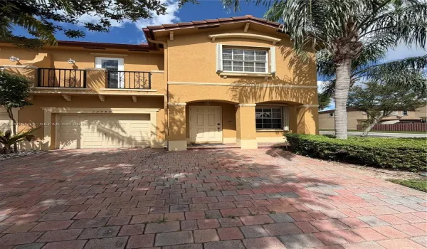 Stucco exterior featuring a paved driveway, covered entryway with arched columns, and a second-story balcony with metal railings