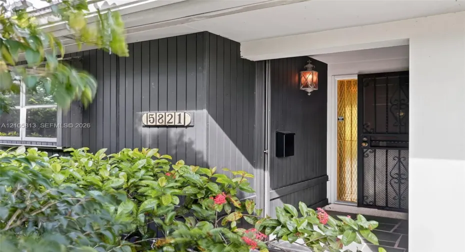 Entryway featuring vertical charcoal-toned siding, a decorative wrought-iron screen door, a traditional wall-mounted lantern, and a stone-tiled porch
