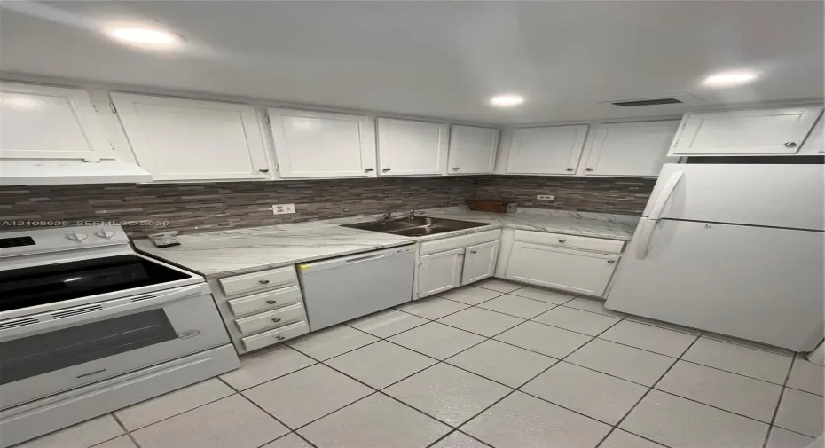 Kitchen featuring white cabinetry, stone-patterned countertops, a decorative tile backsplash, recessed lighting, and tile flooring