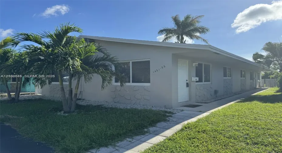 Single-story exterior featuring light-toned stucco walls, horizontal sliding windows, stone-veneer accents, and a paved walkway