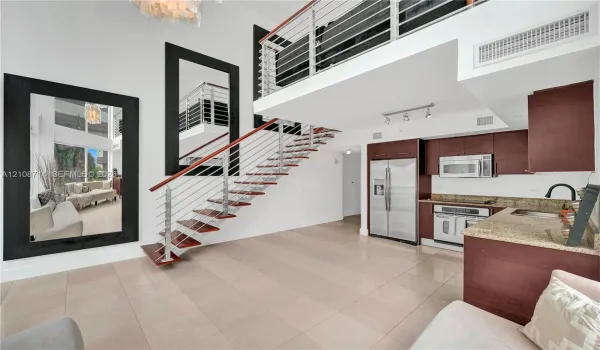 Double-height living area featuring an open staircase with wood treads and horizontal metal railings, tile flooring, built-in cabinetry, and integrated stainless steel appliances